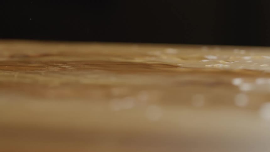A close view shows a light brown wooden surface with scattered pools of shaking water