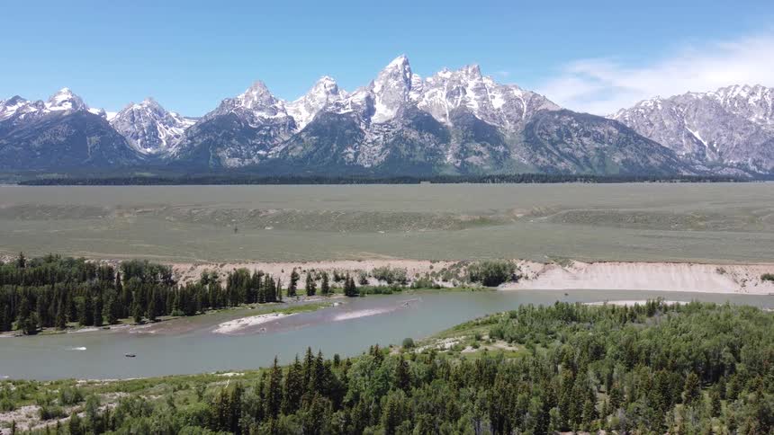 A river and forest are before the large mountain range