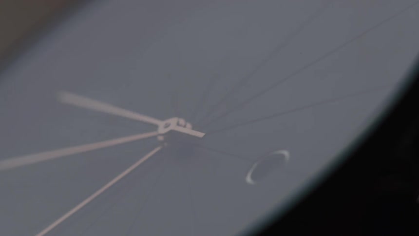 A closeup of a sleek minimalistic watch face shows delicate rosegold hands against a smooth dark background