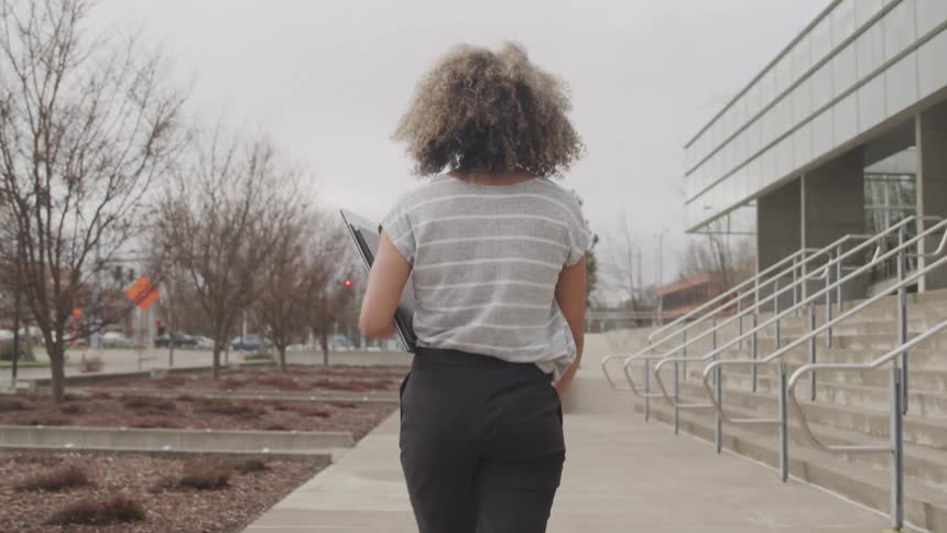 Curly haired woman walking with tablet in outdoor environment