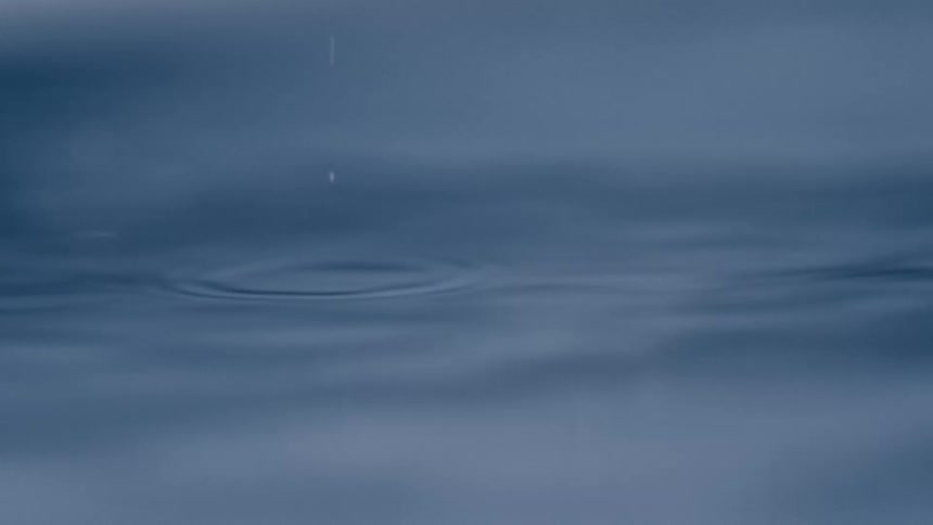 A smooth surface of blue liquid stretches across the frame with faint ripples and a few small droplets disturbing the calm water