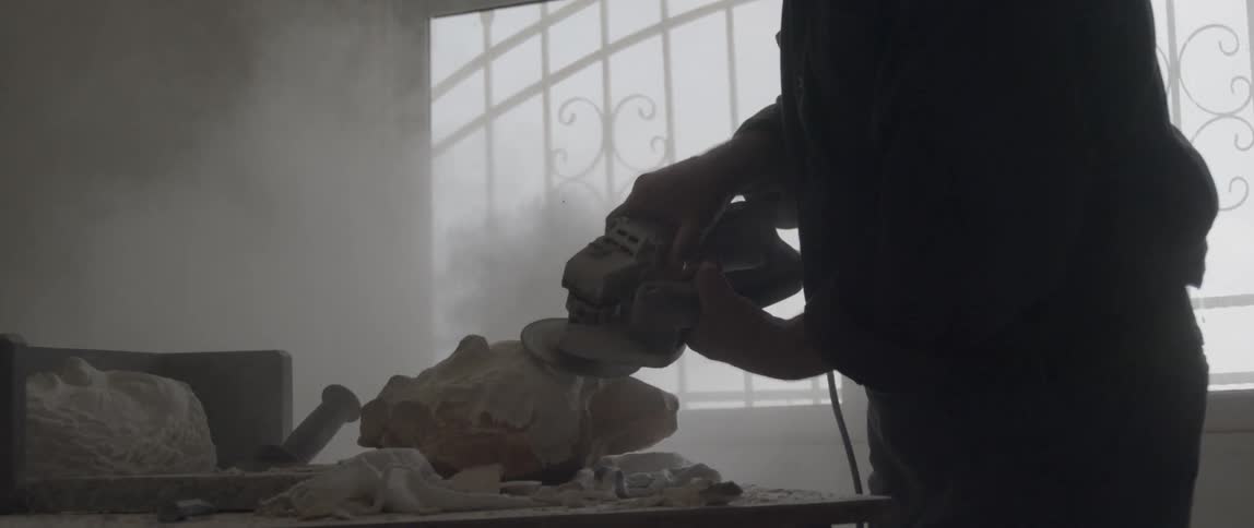 A man is sanding a piece of stone