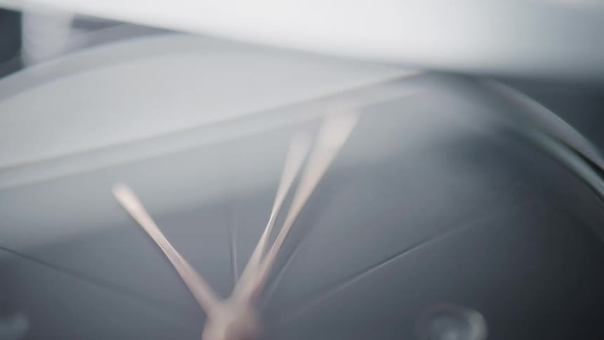 The video provides a closeup abstract shot of a clock face likely a watch with its hands moving rapidly the reflections on the glass surface shift and change creating dynamic light patterns across the frame