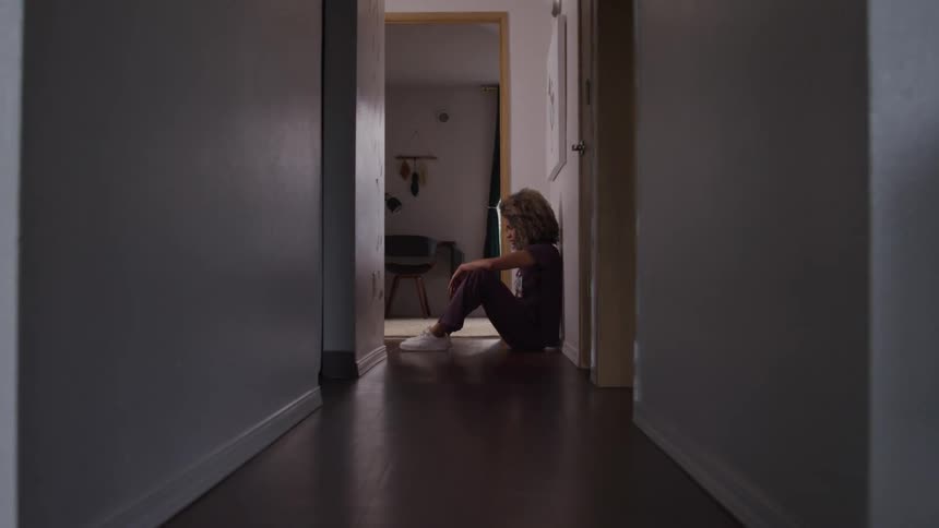 Woman with curly hair sitting on the floor of a hallway