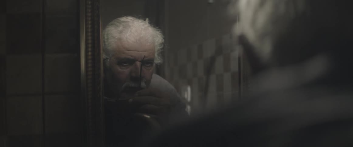 A man takes his glasses off in front of a mirror