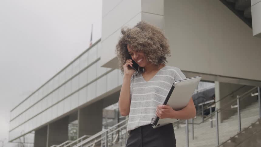 A young black woman makes a phone call while standing on a building stairway entrance during daytime