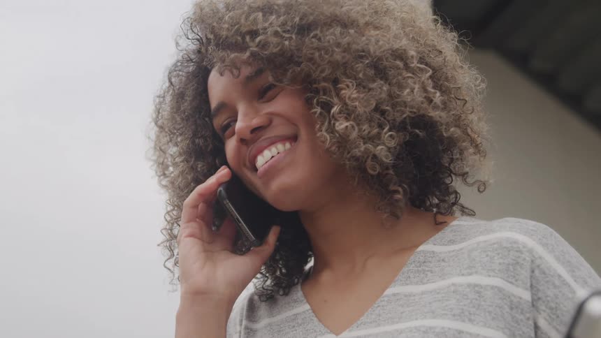 The video shows a woman with curly hair speaking on a phone while smiling she appears to be enjoying the conversation