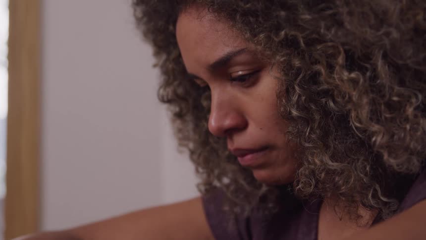 The video features a closeup of a womans face showing her with curly hair and a slightly melancholic or pensive expression her gaze is directed downwards suggesting a moment of reflection or sadness