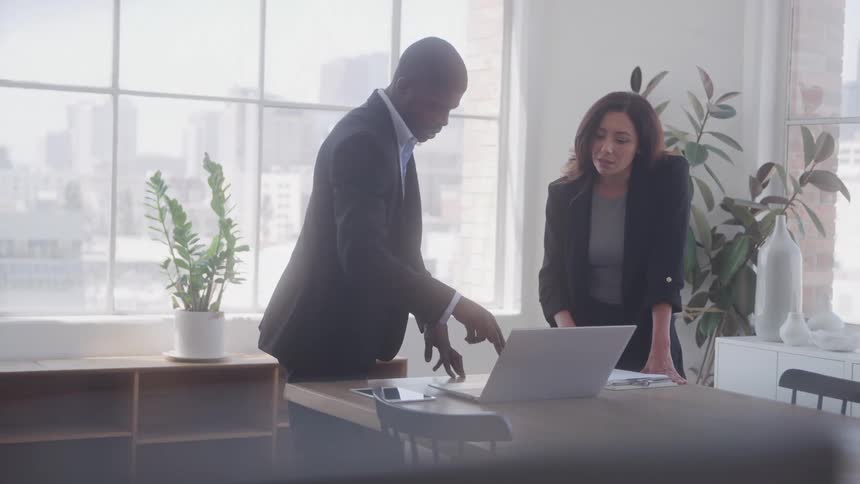 Man and a woman standing in front of a laptop in an office environment talking