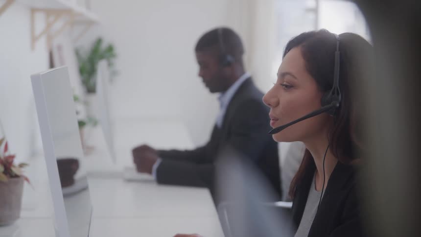 Two sales representatives sitting and wearing headphones talking to customers with computers in front of them