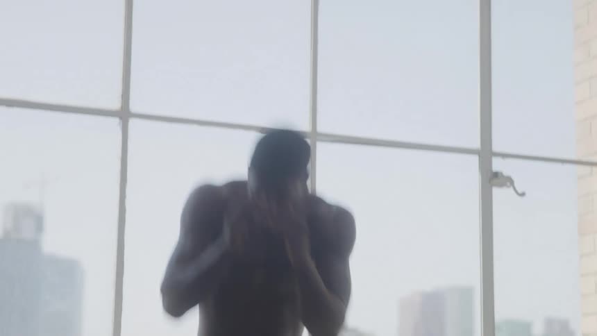 A boxer shadow boxing near a window inside a gym room at midday