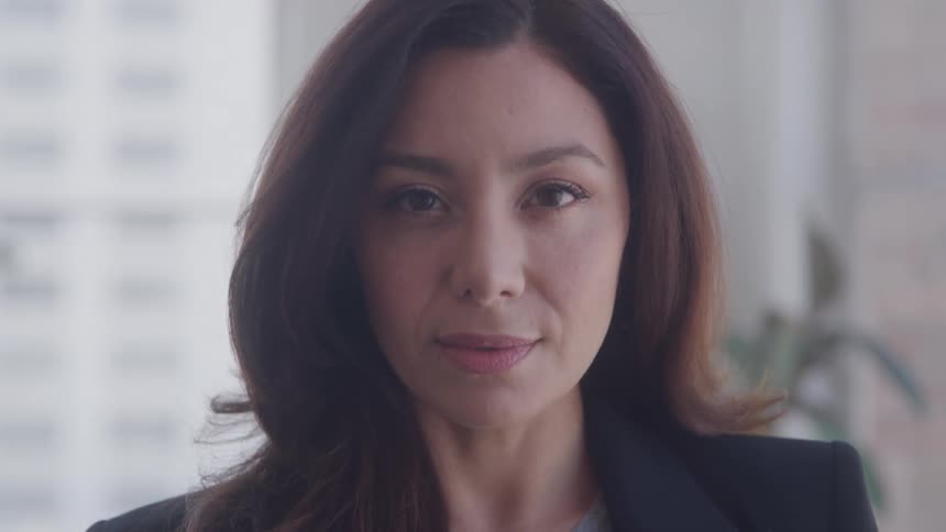 Woman in front of a window in an office turns her head from the right to straight ahead