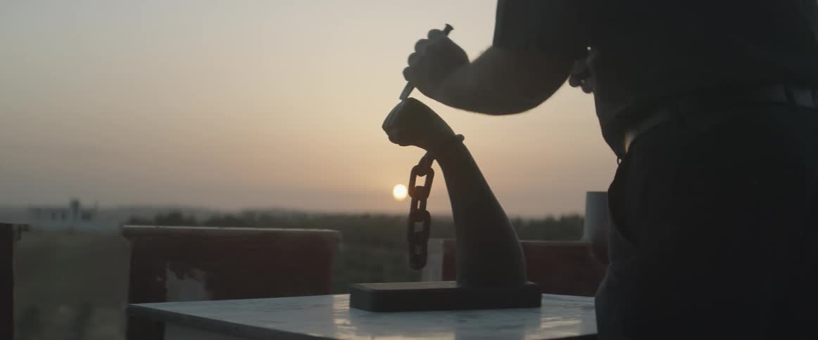 A man carving out a fist shape arm with a chain on it