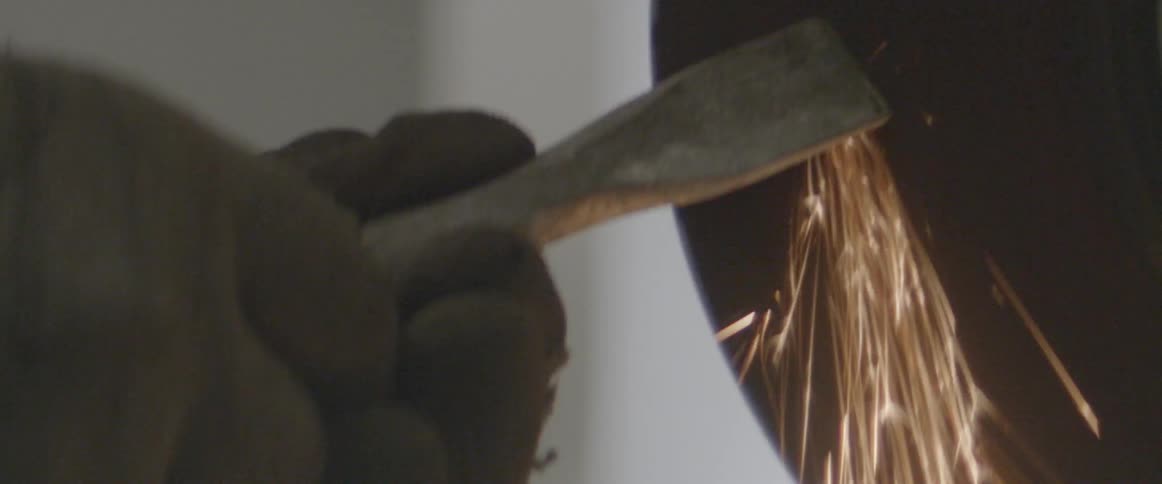 A person is grinding the edge of a chisel causing sparks to fly