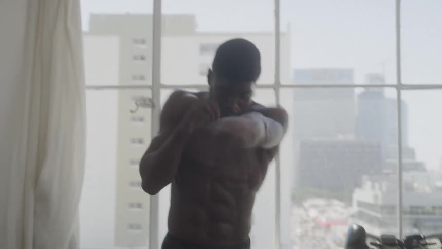 A young man shadow boxing indoors in a gym at midday