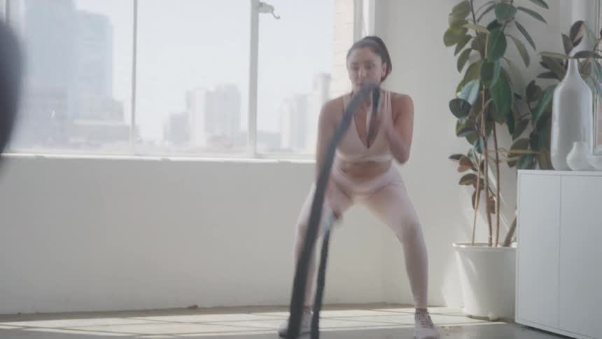 A focused woman works out with battle ropes in a bright indoor setting