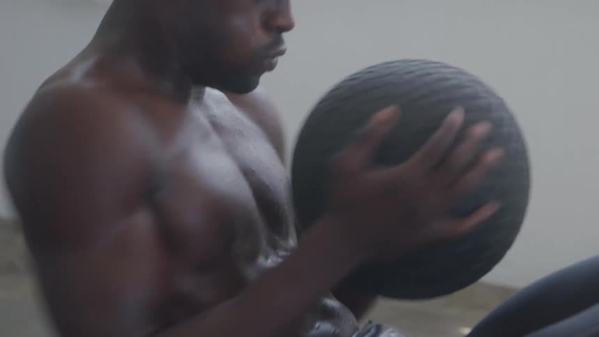 Shirtless man holding a ball doing abdominal training