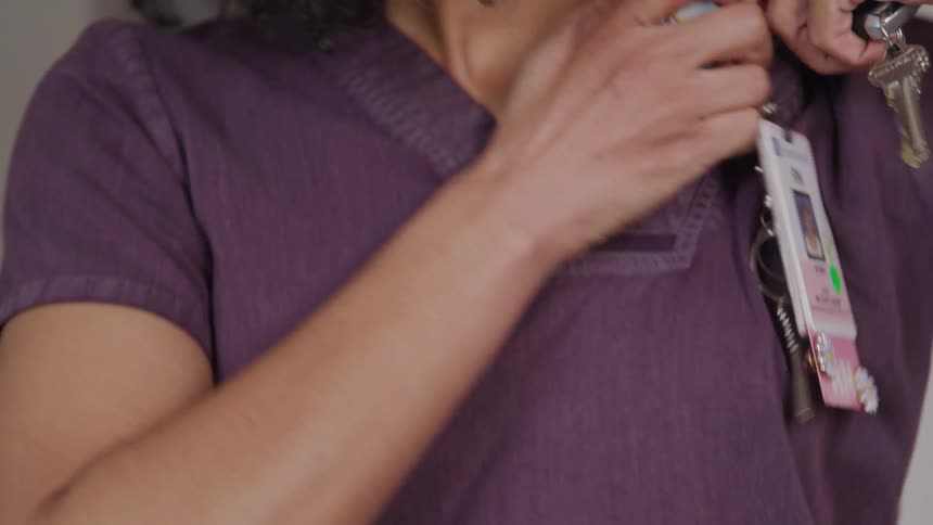 The video begins with a closeup of keys and a card on a dark table then a hand reaches in to pick them up the focus then shifts to show a person partially obscured holding the keys and an id badge that reads rn staff nurse with a picture of a woman