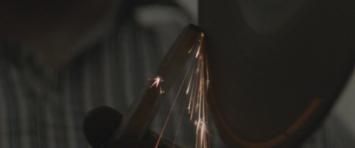 A rotating blade sharpens a chisel as sparks fly through the air