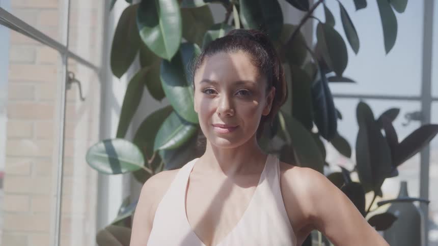 Woman standing near a window with a slight smile receiving sunlight