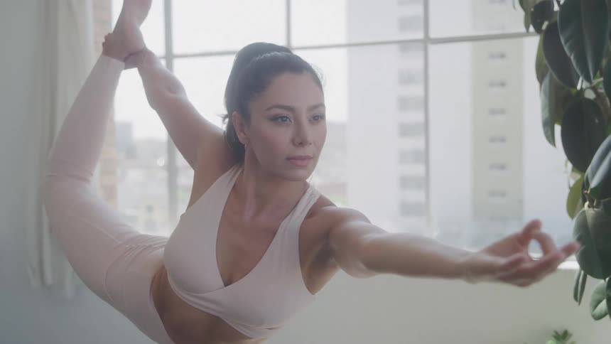 Woman holding a onelegged yoga pose in front of vast windows