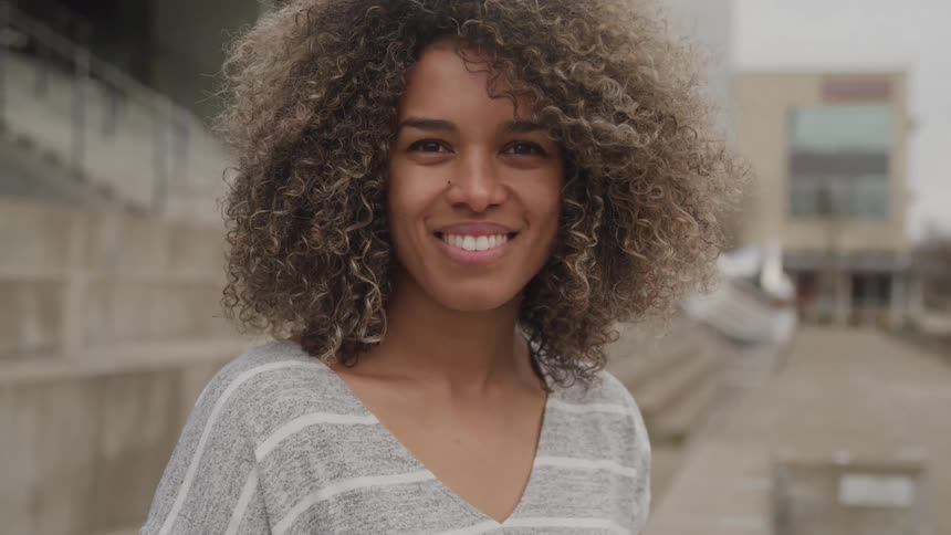 Close up portrait of a young black woman standing outdoors in front of a building stairway during daytime