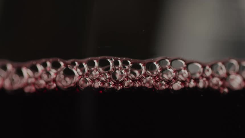 Bubbles in a dark red wine liquid in a glass goblet