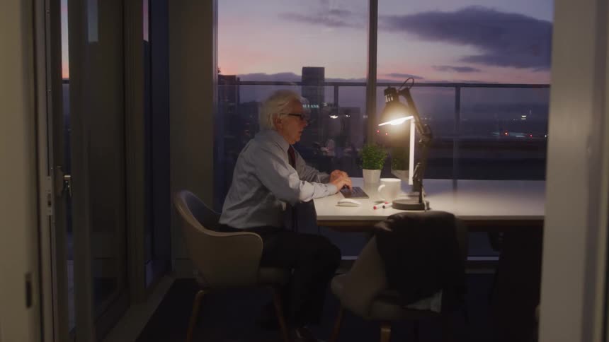 Elderly man working at night in an office room