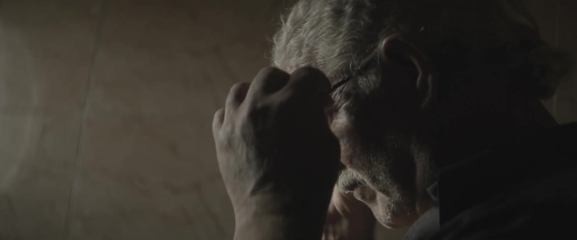 An elderly man puts his glasses on