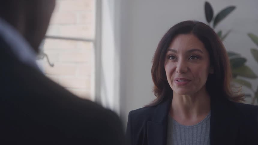 A woman in a suit talks to a male colleague inside the office at midday