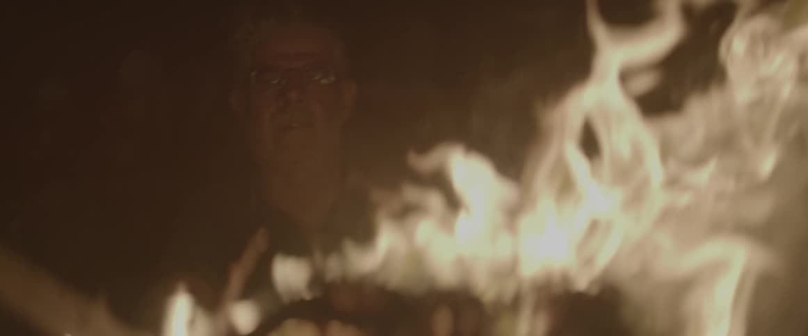 A man sits by a fire outside at night