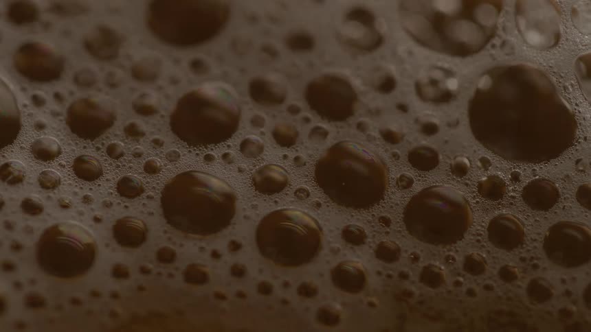 Large and small bubbles cluster on the surface of a dark foamy liquid