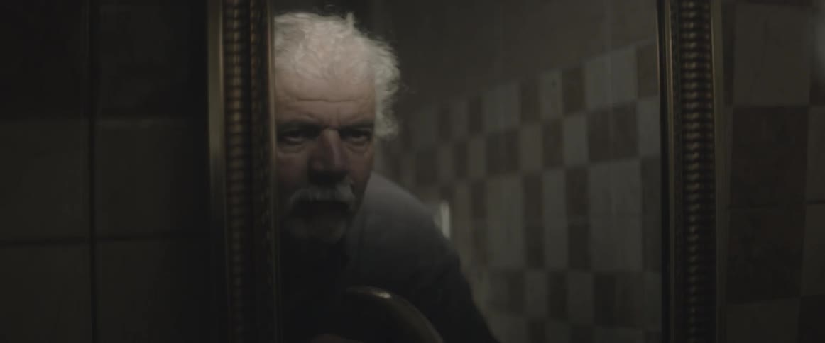 An elderly man looks into a mirror at his reflection