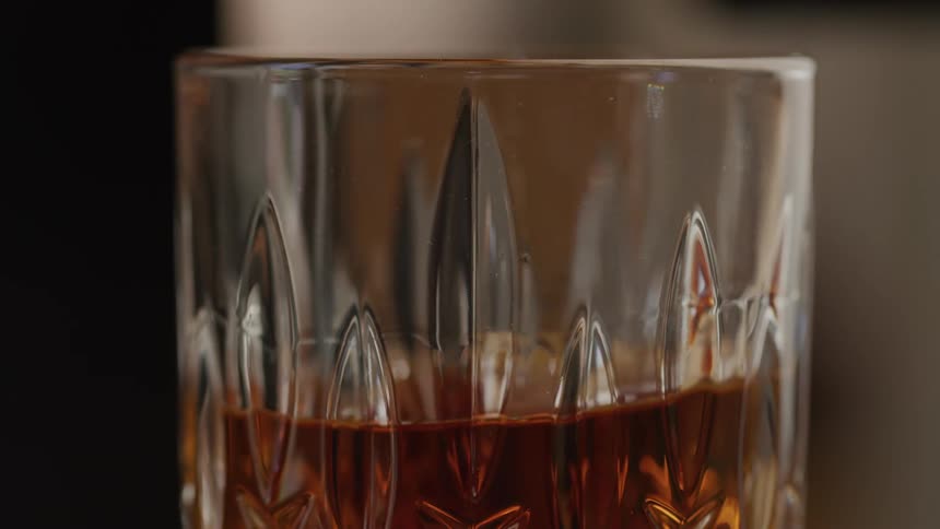 A hand places a glass drink with amber colored liquid down on a surface