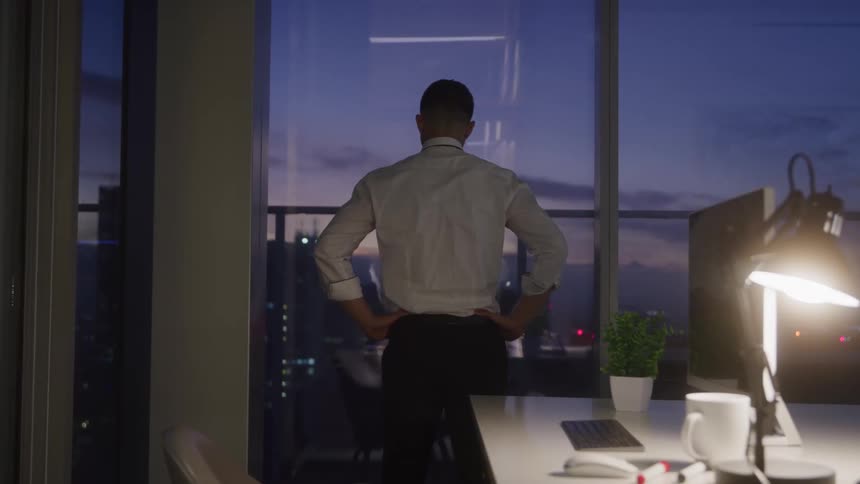 A man is looking out the window in the office as the sun sets