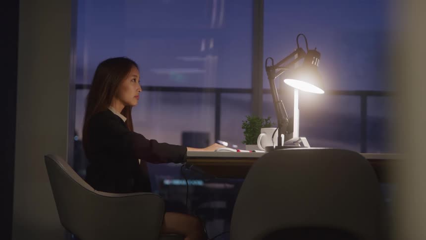 Woman sitting at an office desk at night looking thoughtful
