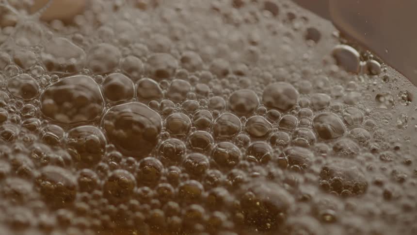 Bubbling liquid is poured forming a dense surface of golden foam
