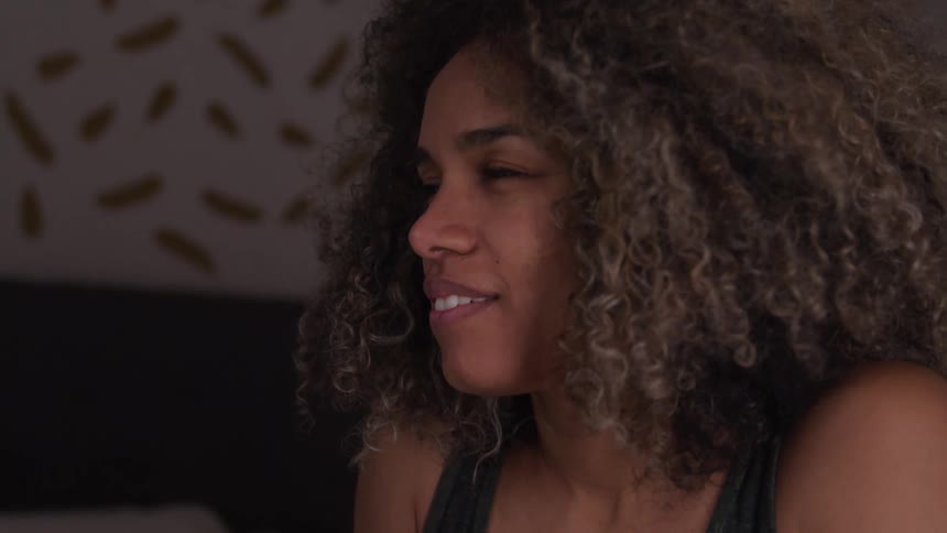 The video features a woman with curly hair initially covering her mouth with her hands appearing distressed over the course of the clip her expression changes to one of relief or happiness as she removes her hands and smiles