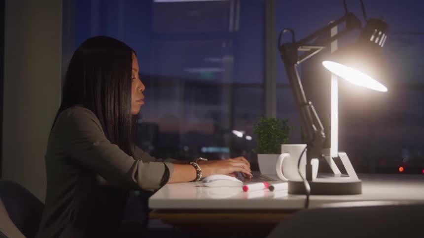 A woman works late at night on a computer in a dimly lit office
