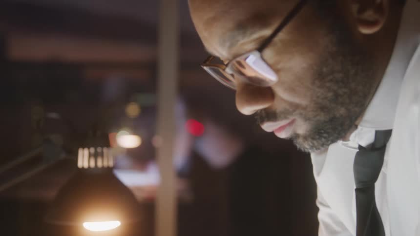 Close up of a black man working at a desk in an office at night