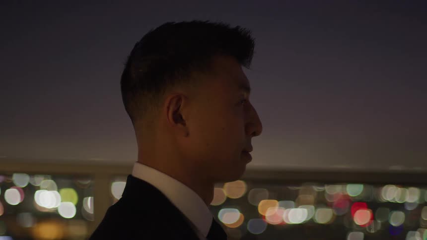 The video shows a man in profile possibly wearing a suit against a dark background outoffocus city lights create a bokeh effect in the background suggesting it is nighttime