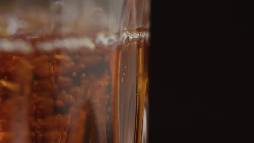 Golden liquid swirls around spices in a clear glass against a dark background