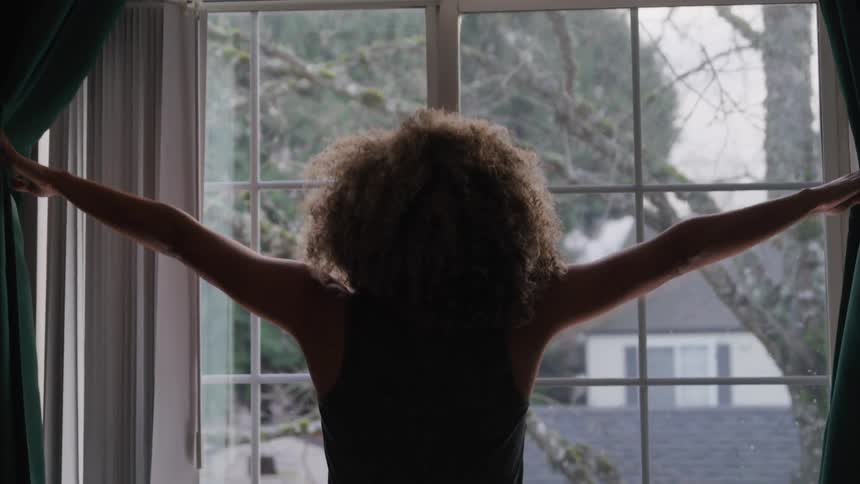 Woman with curly hair opening the bedroom curtain