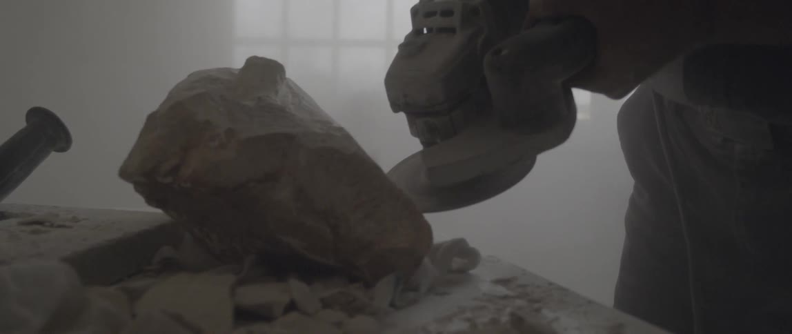 A man is using a large sander to sculpt some stone