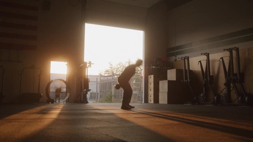 A man working out with a dumbbell in a gym at sunset