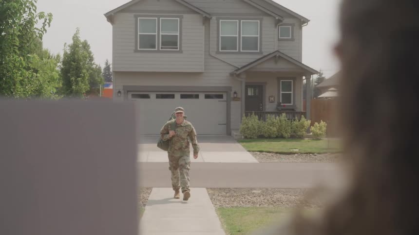 A soldier walks up the driveway toward a suburban home