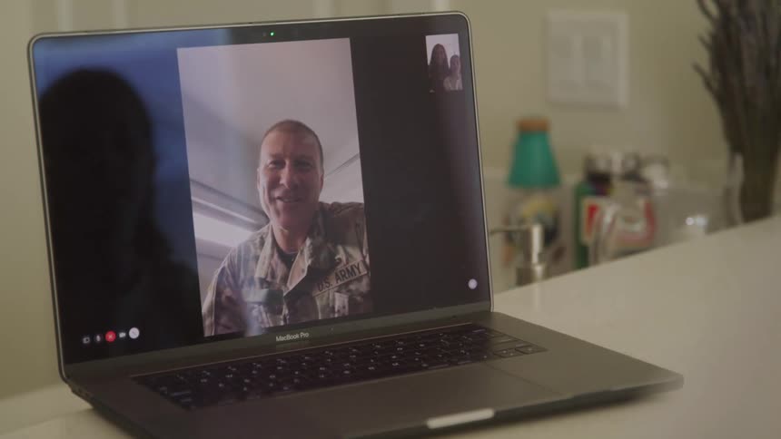 A person in a us army uniform is seen on a video call displayed on a macbook pro laptop the person on the call is smiling and appears to be waving