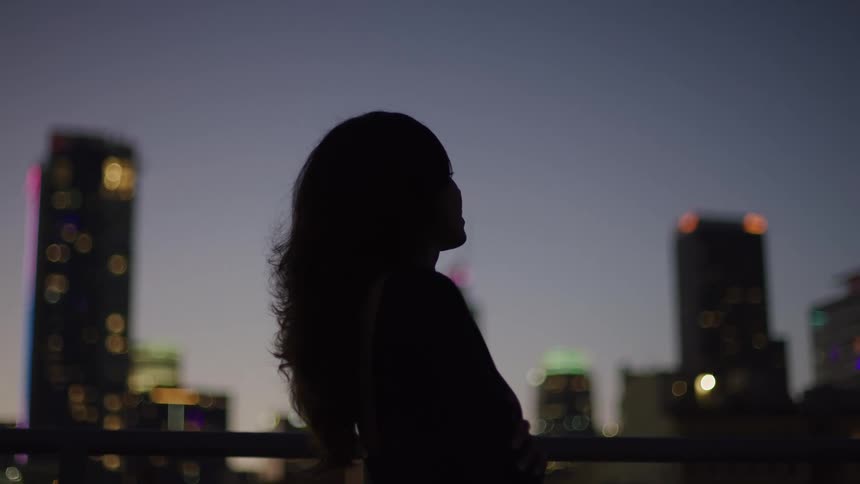 Silhouette of a woman on a terrace with buildings in the background at night