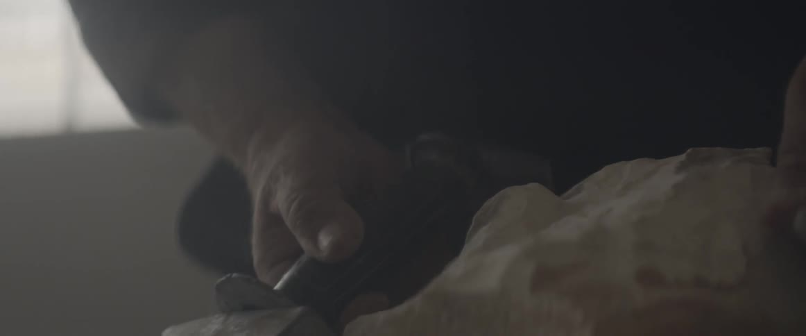 A man uses a hammer and chisel to shape a stone