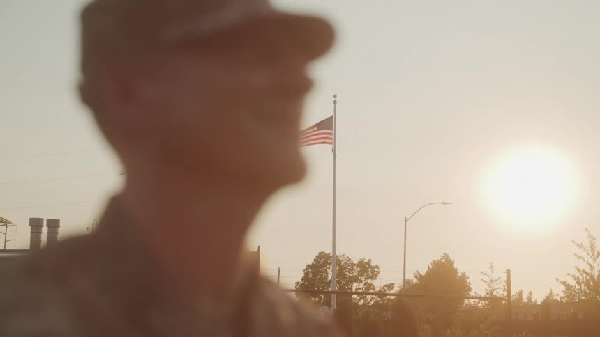 A military officer standing outdoors in a parade with the american flag flying behind him